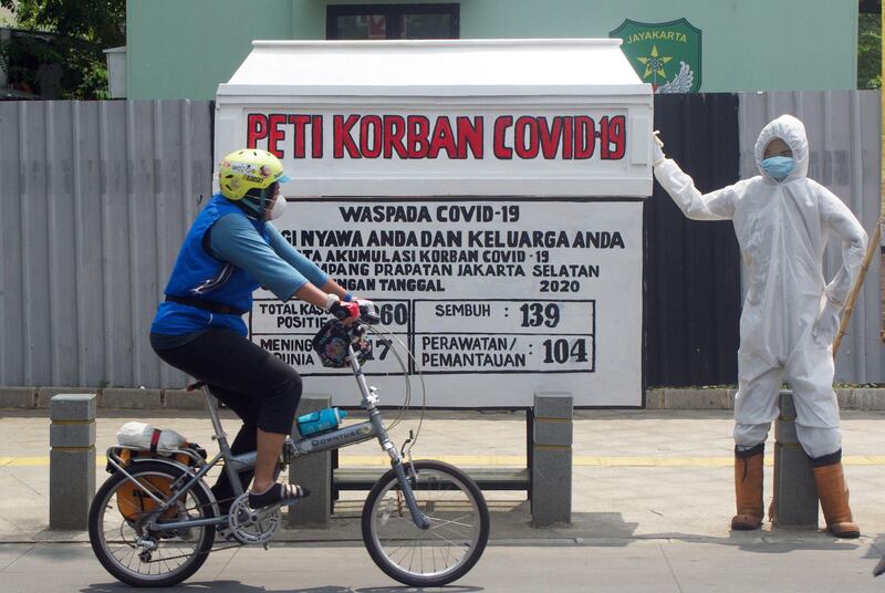 A man rides a bicycle past a replica of a coffin reading "Covid-19 victim's coffin" as an appeal to residents to be more aware of the coronavirus in Jakarta, Indonesia. EPA