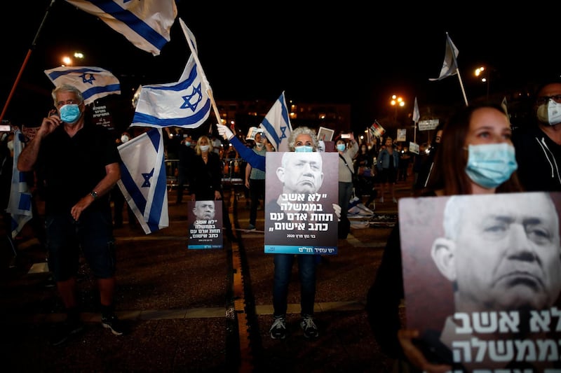 Israelis hold posters with the picture of Benny Gantz, head of the Blue and White party, that read: "I would not sit in a government under a man with criminal indictment", as they protest against Israel's Prime Minister Benjamin Netanyahu, under strict restrictions made to slow down the coronavirus  spread, on Rabin Square in Tel Aviv, Israel April 19, 2020. REUTERS