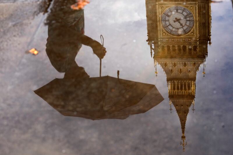 A pedestrian with an umbrella and Big Ben are reflected in a puddle near the Houses of Parliament, in central London. AP