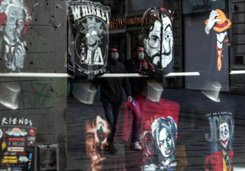 People wearing face masks are reflected in a shop window as they walk in empty Istiklal Street in Istanbul.  EPA