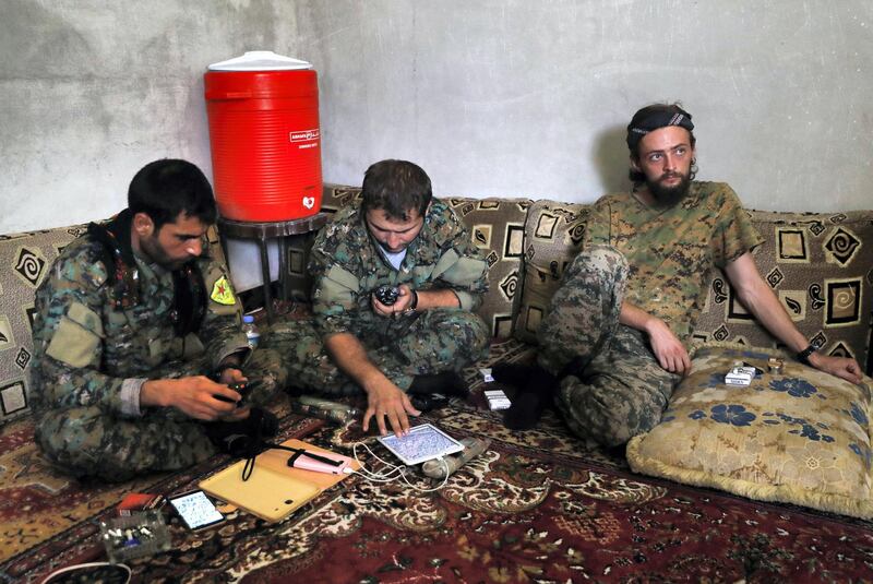 In this picture taken on July 18, 2017, a British man identified as Jac Holmes, right, who had been fighting with U.S.-backed Syrian Democratic Forces (SDF) against Islamic State group, sits on the ground next to two Kurdish commanders at a front line base, in the northern city in Raqqa, Syria. A statement issued Wednesday, Oct. 25, 2017 by the YPG said Holmes, a 24-year-old from Bournemouth, had been battling IS with the YPG since January 2015 when he  died on Monday while clearing mines. (AP Photo/Hussein Malla)