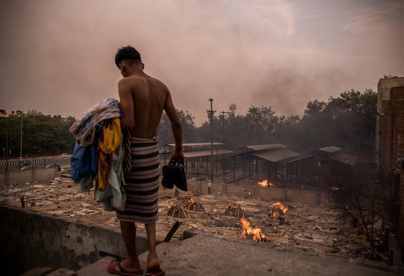 A man does his household chores on the backdrop of burning funeral pyres of Covid-19 victims at a crematorium in New Delhi, India. Anindito Mukherjee/Getty Images