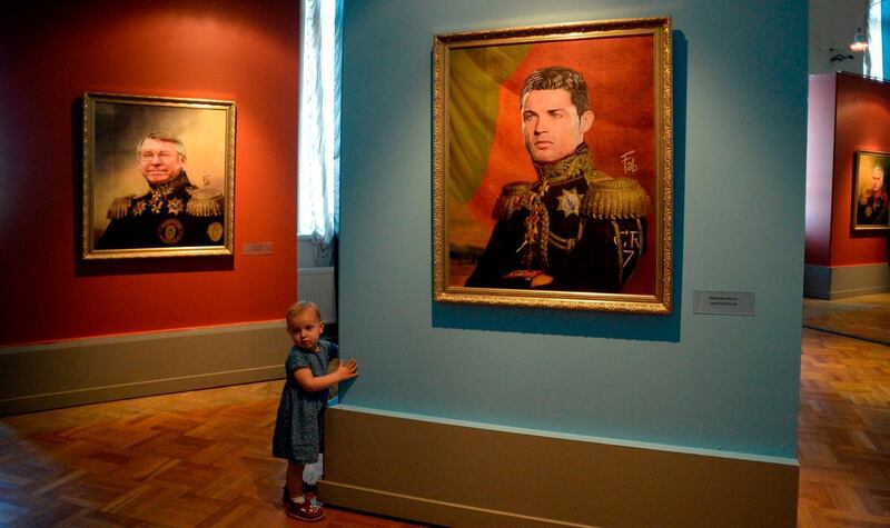 A child walks in front of a portrait of Sir Alex Ferguson (L) and Portugal player Cristiano Ronaldo (R) as they attend during the Art Project 'Like the Gods', presented by the Museum of the Russian Academy of Arts and Birimbelli during the FIFA World Cup of Russia 2018 in Saint Petersburg. Olga Maltseva / AFP