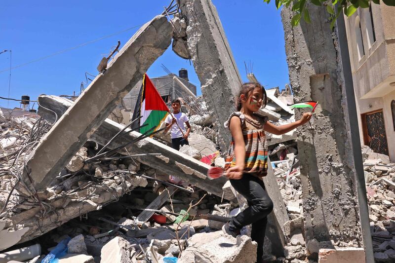 Palestinian children wave Palestinian national flags as they play among the rubble of  buildings destroyed by last month's Israeli bombardment of the Gaza Strip, in Khan Yunis, in the southern Gaza Strip on June 19, 2021. / AFP / SAID KHATIB
