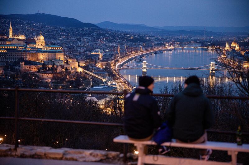 Visitors look out over the city skyline and the Chain Bridge at night in Budapest, Hungary, on Tuesday, March 9, 2021. Prime Minister Viktor Orban severely tightened curbs, closing schools and nearly all retail outlets from Monday. Photographer: Akos Stiller/Bloomberg