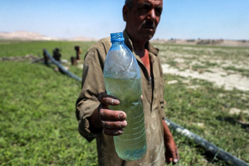 A man holds a water bottle while standing near a pump drawing water from shallows of the Lake Assad reservoir by the town of Rumaylah in eastern Syria, as the area experiences unprecedented lower water levels. AFP