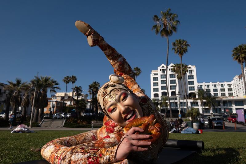 A Cirque du Soleil contortionist takes a bite of a pretzel as she poses for a photo at Santa Monica Beach, California. AP