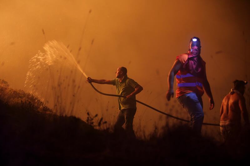 Volunteers use a water hose to fight a wild fire raging near houses in the outskirts of Obidos, Portugal. Armando Franca / AP Photo
