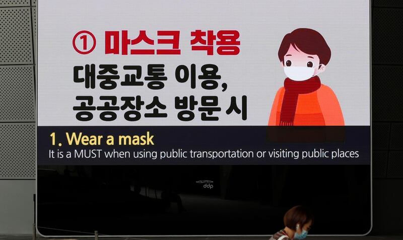 A woman wearing a face mask sits near a screen displaying precautions against the coronavirus in Seoul, South Korea. AP Photo