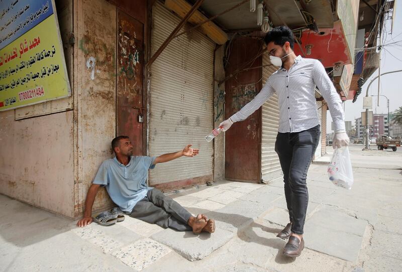 An Iraqi man wearing a protective face mask and gloves gives a bottle of water to a homeless man, who sits in front of a closed shop during a curfew imposed to prevent the spread of coronavirus disease (COVID-19), in Basra, Iraq. REUTERS