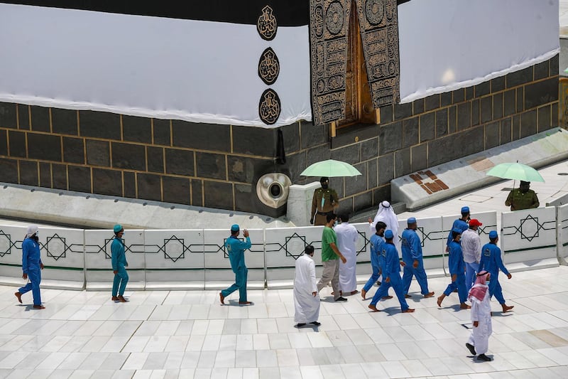 Workers at the the Grand Mosque complex in Saudi Arabia's holy city of Mecca, mask-clad due to the COVID-19 coronavirus pandemic, wave and speak to a security guard as they walk around the the Kaaba, Islam's holiest shrine, at centre of the complex ahead of the annual Hajj pilgrimage season.  AFP
