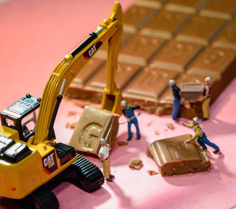 Workmen use a digger and shovels to lift up a square of chocolate. The caption beneath the image reads: "Very good business in the chocolate trade". Courtesy Omar Maree Humaid