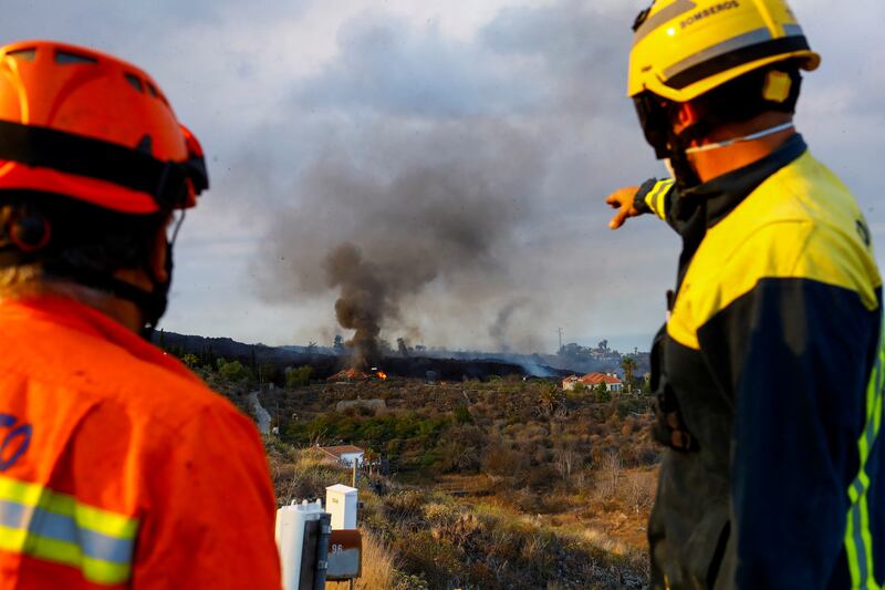 A member of La Palma's Civil Protection team and a firefighter watch as a house burns in the Cumbre Vieja National Park. Photo: Reuters