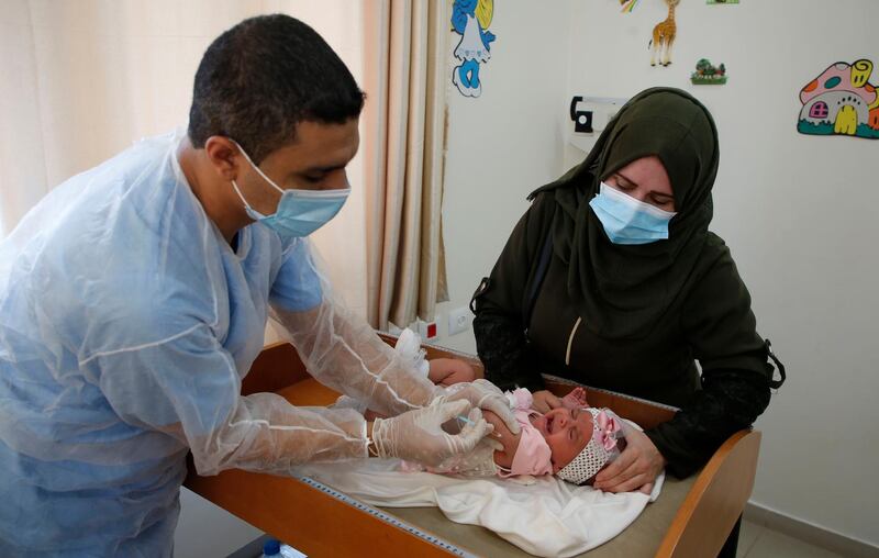 A UN refugee agency employee wearing face mask to protect against the coronavirus pandemic gives polio vaccine to a child at a clinic in Bureij refugee camp in Gaza Strip.  AFP