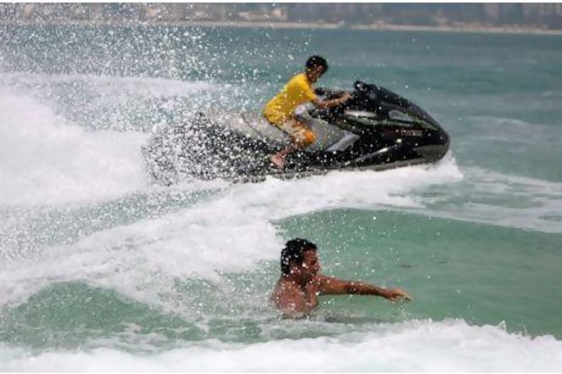 A jet skier rides his machine near a beach in Abu Dhabi very close to a man who is trying to swim, a situation which many say is a danger and should be illegal. Sammy Dallal / The National