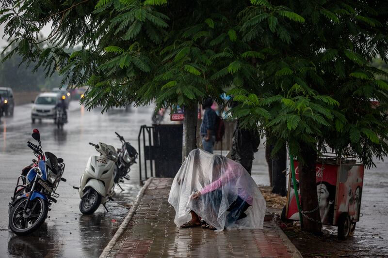 A roadside vendor and motorcyclists take shelter from the rain under a plastic sheet in Noida, a suburb of New Delhi, India.
