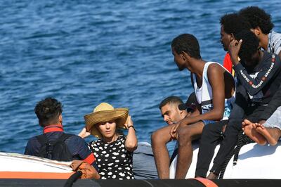 A migrant woman wearing a straw hat is seen with other migrants from Tunisia and Lybia as they arrive onboard of an Italian Guardia Costiera (Coast Guard) boat in the Italian Pelagie Island of Lampedusa, on August 1, 2020. / AFP / Alberto PIZZOLI
