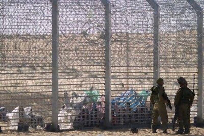 African refugees sit on the ground behind a border fence after they attempted to cross illegally from Egypt into Israel as Israeli soldiers stand guard near the border with Egypt.