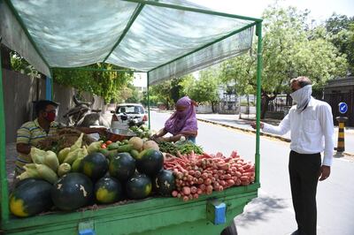 A vegetable vendor (L) serves customers during a government-imposed nationwide lockdown as a preventive measure against the COVID-19 coronavirus, in Ahmedabad on April 10, 2020.  / AFP / SAM PANTHAKY
