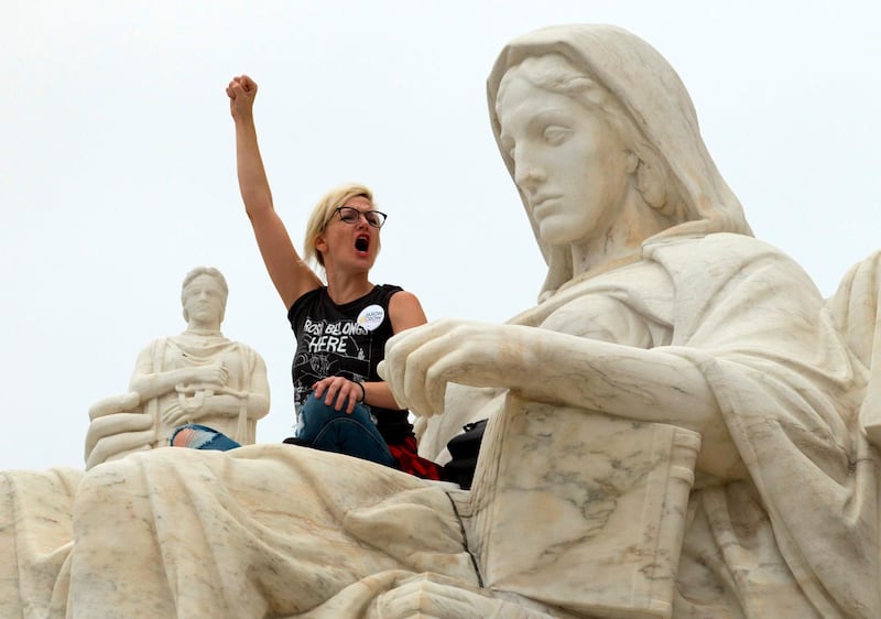 TOPSHOT - Demonstrator Jessica Campbell-Swanson of Denver, stands on the lap of the "Contemplation of Justice" statue as protestors take the steps of the US Supreme Court protesting against the appointment of Supreme Court nominee Brett Kavanaugh at Capitol Hill in Washington DC, on October 6, 2018. / AFP / Jose Luis Magana
