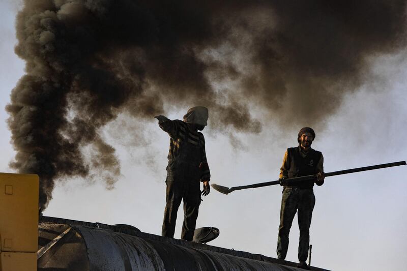 Men work at a makeshift oil refinery near Tarhin, in Aleppo, Syria, as black smoke billows behind them. Areas surrounding such refineries are left with contaminated groundwater and agricultural land. AFP