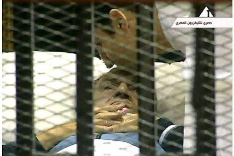 Egyptian president Hosni Mubarak is kissed by his son Alaa as he lies on a bed in a cage during his trial Monday.