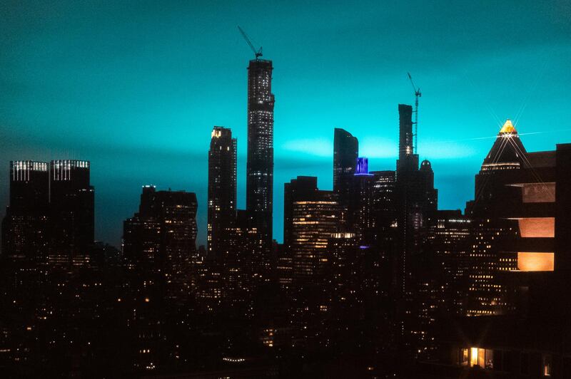 Buildings stand as the night sky is illuminated by blue light in New York. Bloomberg