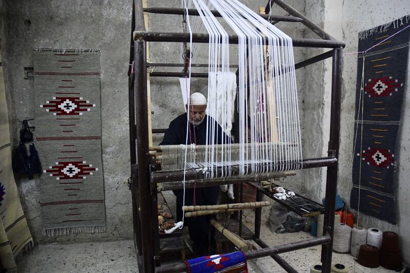 Abdel Kader Khosayyem, 70, a traditional kilim weaver, works at his workshop in the northern Syrian city of Aleppo, on April 20, 2022.  - Khosayyem's family has been weaving kilims since about 400 years.  He has been teaching his skills to his children relatives, with the hope of keeping the family tradition alive.  (Photo by AFP)