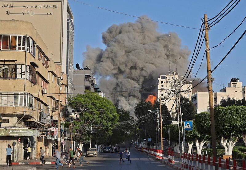 People run away from the vicinity of Al-Sharouk tower as it collapses after being hit by an Israeli air strike, in Gaza City, on May 12, 2021. An Israeli air strike destroyed a multi-storey building in Gaza City today, AFP reporters said, as the Jewish state continued its heavy bombardment of the Palestinian enclave. AFP