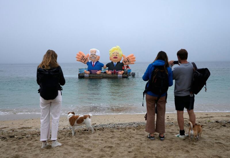 People watch from the beach as two giant balloons, depicting US President Joe Biden and British Prime Minister Boris Johnson, float on a dock in the harbour of Falmouth, Cornwall. AP Photo