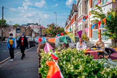 People wearing protective face masks walk past Walthamstow residents having a street party in their front garden to celebrate the 75th anniversary of VE Day (Victory in Europe Day), the end of the Second World War in Europe in Walthamstow in East London, May 8. Tolga Akmen / AFP 