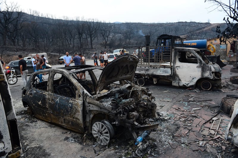 Algerians gather next to vehicles destroyed by wildfires in Bouira, 100km from the capital, Algiers. AP