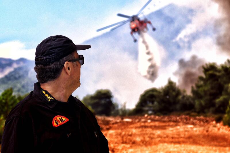 A fireman watches a helicopter which tries to extinguish a wildfire raging in Verori, near Loutraki city, Peloponnese. EPA