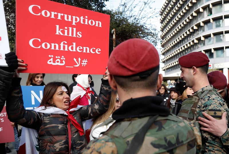 FILE - In this February 11, 2020 file photo, an anti-government protester shouts slogans as she holds a placard in front of Lebanese army soldiers, in downtown Beirut, Lebanon, Lebanon's government agreed Tuesday to hire a New York-based company to conduct a forensic audit of the country's central bank accounts to determine how massive amounts of money were spent in the nation plagued by corruption. (AP Photo/Hussein Malla, File)