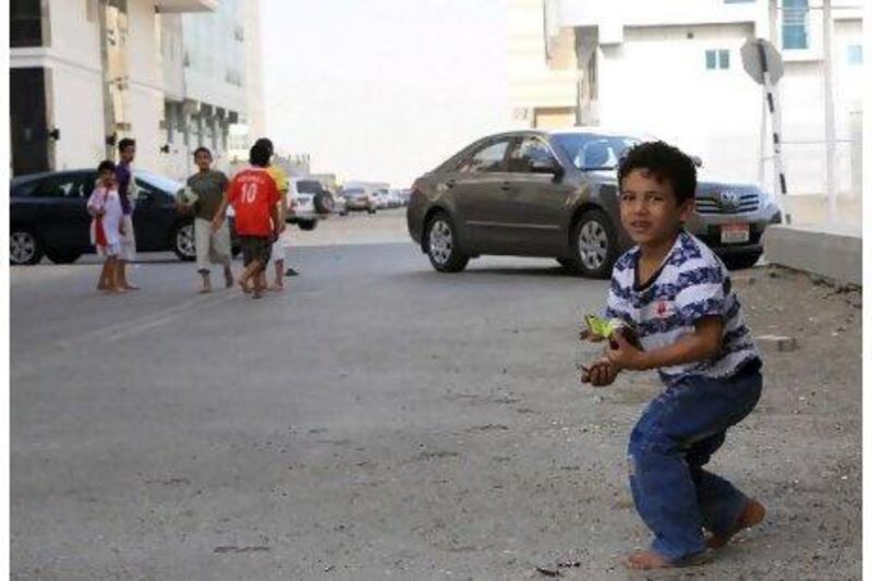 A boy clears away broken glass before he and his friends start a new game on the streets of Mussaffah. Ravindranath K / The National