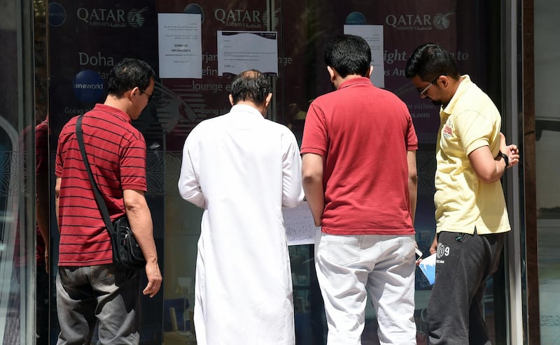 People stand before the offices of the Qatar Airways bureau in Riyadh as they read a paper informing customers of a hotline for complaints, hung below notice signs informing customers that the premises are closed until further notice as per instructions by the Saudi Authority of Civil Aviation, in the Saudi capital on June 7, 2017. (Photo by FAYEZ NURELDINE / AFP)