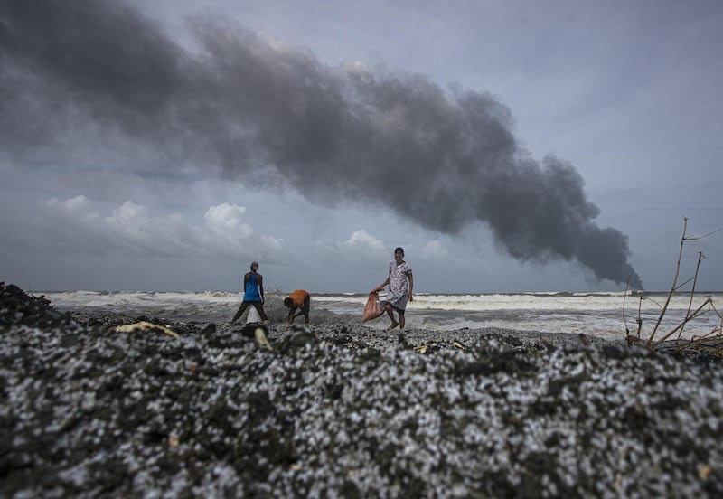 The Singaporean ship 'MV X-Press Pearl' burns in the background as people collect debris from the ship, which is anchored off Colombo port at Kapungoda, near Colombo, Sri Lanka. India this week sent vessels to help douse the blaze. AP Photo