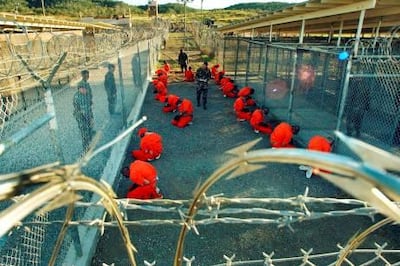 In this photo released 18 January 2002 by the Department of Defense, Al-Qaeda and Taliban detainees in orange jumpsuits sit in a holding area under the surveillence of US military police at Camp X-Ray at Naval Base Guantanamo Bay, Cuba, during in-processing to the temporary detention facility 11 January 2002.  The detainees, captured in Afghanistan during Operation Enduring Freedom, are given a basic physical exam by a doctor, to include a chest x-ray blood samples drawn to assess their health.  AFP PHOTO / US NAVY / Shane T. McCOY