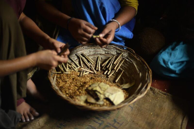Women sit with a basket filled with tobacco flakes and cotton thread, materials used to roll bidis.
