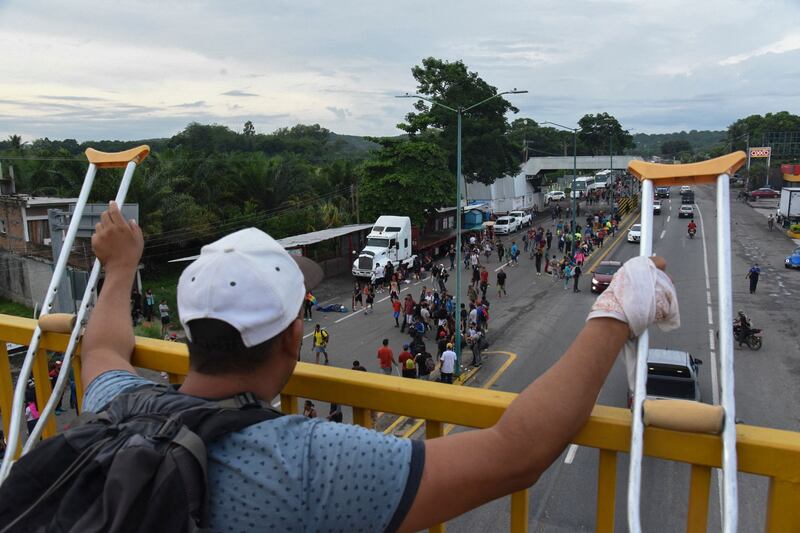 A Venezuelan migrant using crutches looks on as other Latin American migrants pass by in Huehuetan. AFP