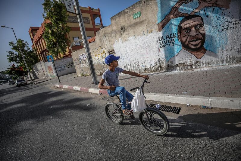 A Palestinian boy rides his bicycle next a mural of George Floyd in Gaza City.  EPA