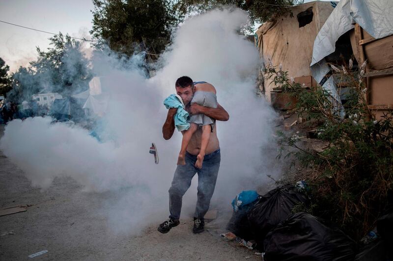 TOPSHOT - A man holds a boy during clashes with police outside the refugee camp of Moria on the Greek island of Lesbos, on September 29, 2019. At least one migrant died on September 29, 2019, after a fire broke out in Moria, the over-crowded refugee camp on the Greek island of Lesbos, Greece's Health Ministry said. Police were firing tear gas to control crowds who started rioting after the fire ignited inside the camp, according to an AFP correspondent. / AFP / ANGELOS TZORTZINIS
