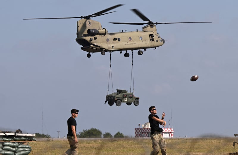 A Boeing Chinook helicopter of the US Army's 101st Airborne Division transports a military vehicle while in the foreground military personnel play American football during a demonstration drill at Mihail Kogalniceanu Airbase near Constanta, Romania.  AFP