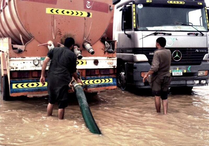 Men work to pump away flood water on the E11 in the Western Region. (Sammy Dallal / The National)  