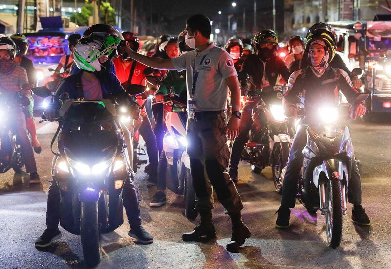 A traffic officer checks temperatures of motorcycle riders at a checkpoint as part of the precautionary measures against the spread of the new coronavirus in Manila. AP