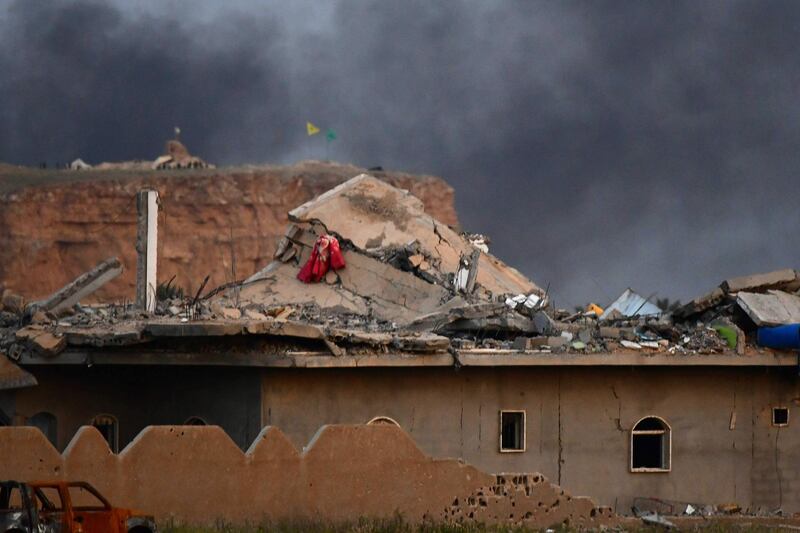 The damaged roof of a building with smoke rising over the village of Baghouz in the eastern Syrian province of Deir Ezzor, with the flags of the Kurdish People's Protection Units (Yellow) and Women's Protection Units (Green) seen flying at one of their positions in the background.   AFP