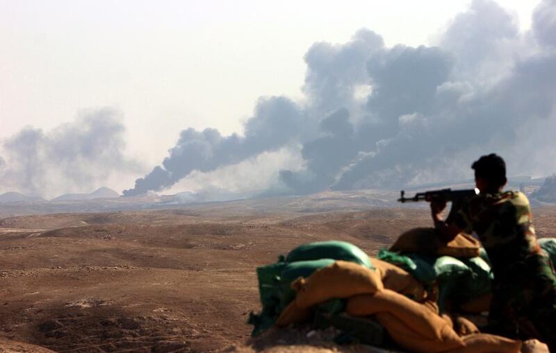 An Iraqi soldier poses with his weapon as smoke rising from the Ajeel oil field near Baiji city, northern Iraq. The IMF has called on Gulf states to introduce taxes, trim spending, cut subsidies and introduce reforms to help balance their fiscal budgets.  EPA