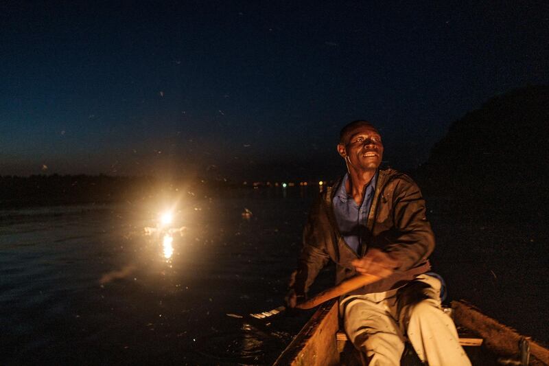 Mukasa rows his boat after setting up a kerosene lamp (behind him) which will eventually attract thousands of small silverfish on the Nile river, in Bujagali, Uganda, on November 12, 2020. - Fishermen in Uganda using more traditional fishing methods have been struggling to financially sustain themselves due to the lack of clients, which was caused by several lockdowns imposed to curb the spread of COVID-19 coronavirus since early March 2020. (Photo by Sumy Sadurni / AFP)