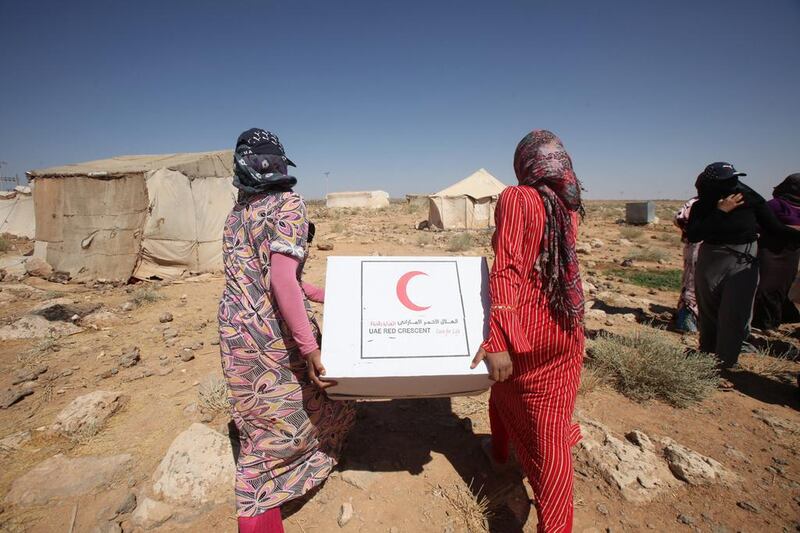 Syrian refugees carry off aid handed out by Emirates Red Crescent as they head to their tent in north-east Jordan, near the border with Syria. Salah Malkawi / The National