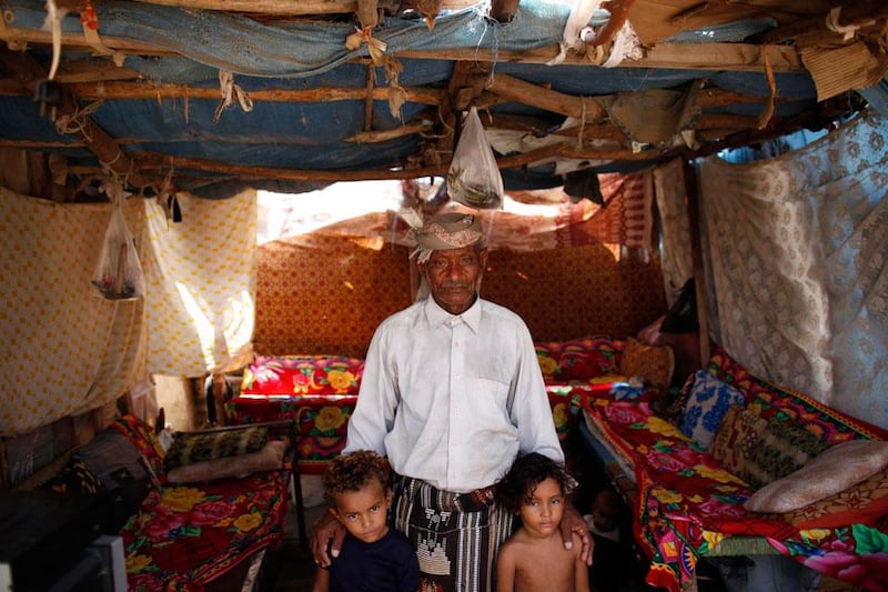 A man poses for a photo with his grandchildren in their hut in a slum area.